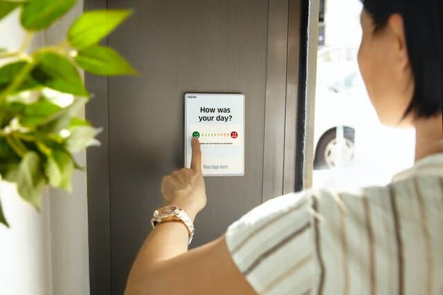 Person pressing a button to give positive feedback on a device asking “how was your day”