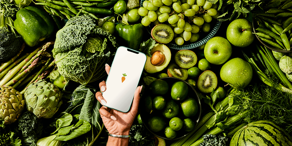 Green fruits and vegetables behind a phone, which features the Instacart logo